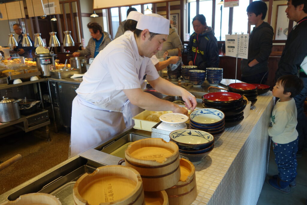 A chef prepares a bowl of udon.